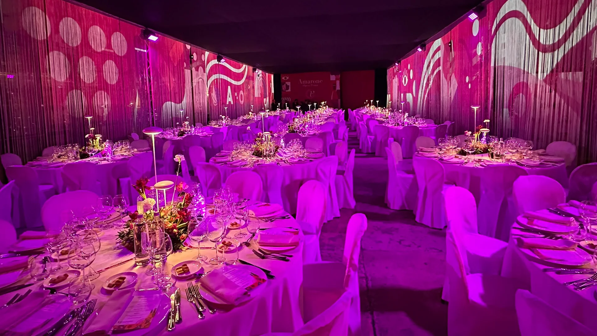 Cena di gala con toni bordeaux e illuminazione immersiva per evento Amarone